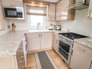 A kitchen with a microwave, sink, kettle, toaster, stove, and cabinets at Yealands 27 South Lakeland Leisure Village near Carnforth