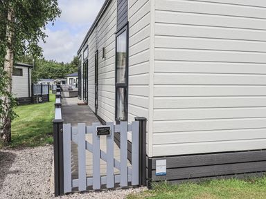 A gate and deck outside a lodge with grass and other lodges at Yealands 27 South Lakeland Leisure Village near Carnforth