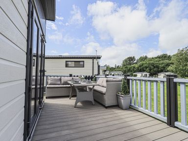 An outdoor deck with a glass table and two sofas surrounded by a fence at Yealands 27 South Lakeland Leisure Village near Carnforth