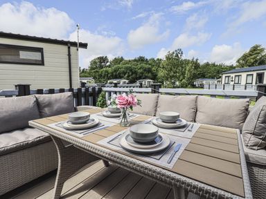 An outdoor dining table set with plates bowls and cutlery on a deck with cushioned seating at Yealands 27 South Lakeland Leisure Village near Carnforth