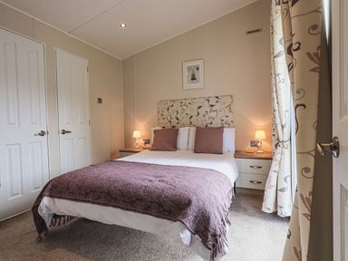 A bedroom with a double bed two bedside tables with lamps curtains and two doors at Yealands 27 South Lakeland Leisure Village near Carnforth