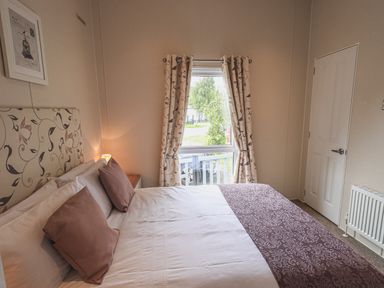 A bedroom with a bed a window with curtains a door and a radiator at Yealands 27 South Lakeland Leisure Village near Carnforth