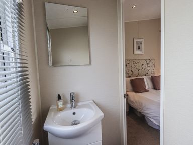 A bathroom sink with a mirror and soap dispenser and a view into a bedroom with a bed at Yealands 27 South Lakeland Leisure Village near Carnforth