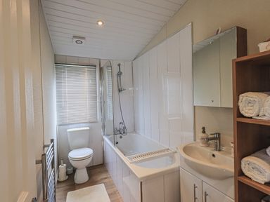 A bathroom with a bathtub shower toilet sink and wooden shelf with towels at Yealands 27 South Lakeland Leisure Village near Carnforth