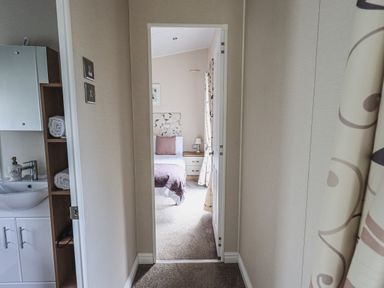 A hallway leading to a bedroom with a bed a nightstand and a lamp at Yealands 27 South Lakeland Leisure Village near Carnforth