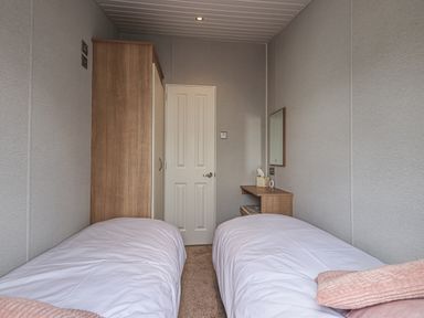 A bedroom with two single beds, a wooden wardrobe, a small desk with a mirror and a stool at Yealands 27 South Lakeland Leisure Village near Carnforth