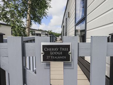 A wooden fence with a sign reading Cherry Tree Lodge 27 Yealands outside a white lodge at South Lakeland Leisure Village near Carnforth