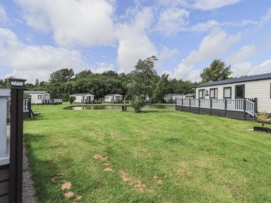 A grassy area with several mobile homes and a small pond under a cloudy sky at Yealands 27 South Lakeland Leisure Village near Carnforth