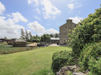 A stone building near a landscaped garden with a gazebo and wooden cabins at Yealands 27 South Lakeland Leisure Village near Carnforth