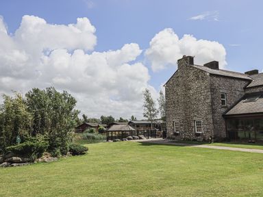 A stone house with a green lawn and garden area under a cloudy sky at Yealands 27 South Lakeland Leisure Village near Carnforth