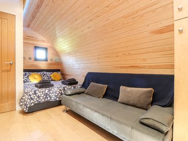 A bedroom with a bed and sofa against wooden walls at Sea View in St Buryan