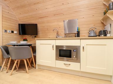 A kitchenette with a microwave oven, sink, kettle, table with chairs and a wall-mounted TV at Sea View in St Buryan