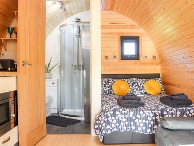 A bedroom with a double bed and yellow pillows next to a bathroom with a shower and toilet at Sea View in St Buryan