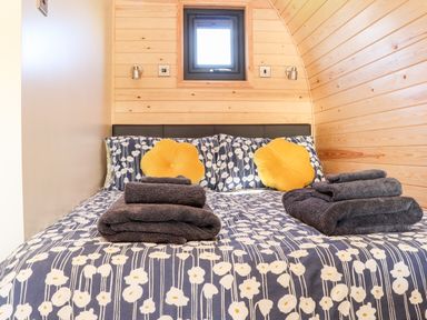 A bed with floral patterned bedding two yellow flower shaped pillows and folded towels on it in a wood paneled room at Sea View in St Buryan
