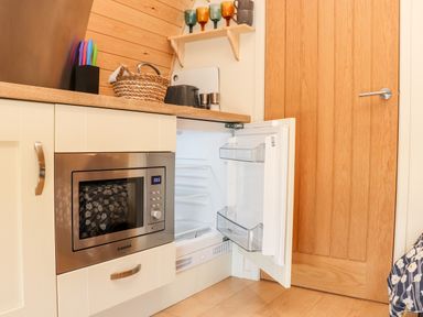 A kitchen area with a built-in microwave and an open mini fridge next to a wooden door with a countertop holding a knife block, basket, toaster, and spice containers