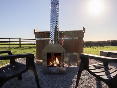 An outdoor hot tub with a wood stove and two black chairs on a gravel surface at Sea View in St Buryan
