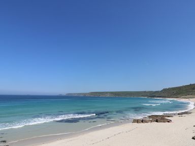 A sandy beach with rocks and waves along the shoreline under a clear blue sky at Sea View in St Buryan