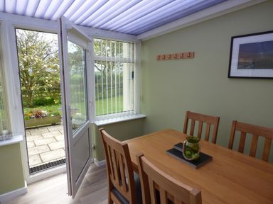 A dining area with a wooden table and chairs next to a door leading to a garden at Hafod Cottage in Cemaes Bay