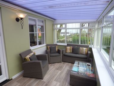 A sunroom with wicker armchairs and a sofa with striped cushions and a glass coffee table at Hafod Cottage in Cemaes Bay
