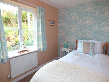 A bedroom with a single bed a bedside table with a lamp a window with curtains and floral wallpaper at Hafod Cottage in Cemaes Bay