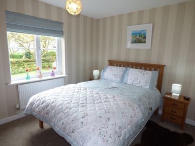 A bedroom with a double bed wooden headboard two bedside tables with lamps striped wallpaper and a window with blue blinds at Hafod Cottage in Cemaes Bay