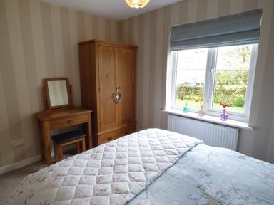 A bedroom with a bed a wooden wardrobe a dressing table and a window with three small vases with flowers at Hafod Cottage in Cemaes Bay