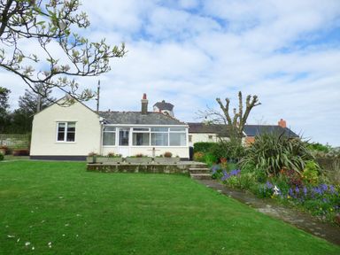 A single story house with a lawn and flower beds in the garden at Hafod Cottage in Cemaes Bay