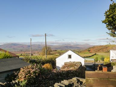 A view of hills and fields with a white building and stone walls under a clear sky at Brookside in Grizebeck