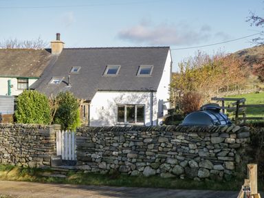 A white house with a slate roof behind a stone wall and a white picket gate at Brookside in Grizebeck