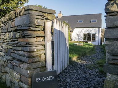 A stone wall with a white wooden gate and a sign reading Brookside with a path leading to a white house at Brookside in Grizebeck