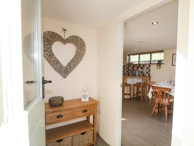 An entryway with a wooden console table and heart-shaped wall decor looking into a dining area with wooden chairs and a table set at Brookside in Grizebeck