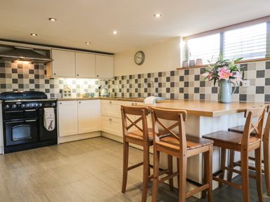 A kitchen with a black oven white cabinets wooden chairs and a wooden countertop with flowers in a vase at Brookside in Grizebeck