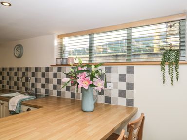 A kitchen with a wooden countertop a vase of pink flowers a sink and tiled backsplash at Brookside in Grizebeck
