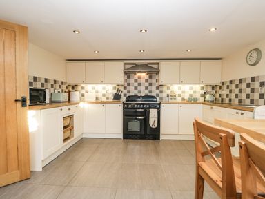 A kitchen with white cabinets a black stove and wooden chairs at Brookside in Grizebeck