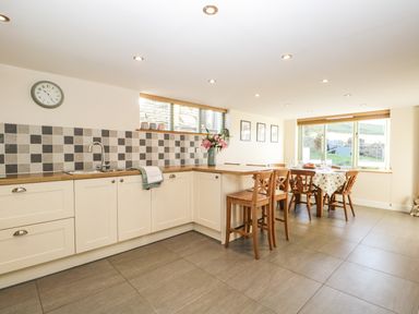 A kitchen with a tiled backsplash, wooden chairs and a dining table by a window at Brookside in Grizebeck