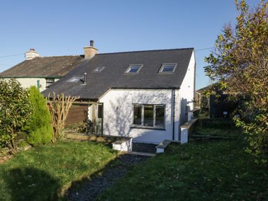A white two story house with skylights and a grassy garden surrounded by trees at Brookside in Grizebeck