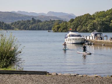 A lake with two people paddleboarding near boats and a dock surrounded by trees and mountains at Brookside in Grizebeck