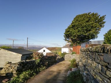 A narrow country lane bordered by stone walls and small sheds with a house and tree in the background at Brookside in Grizebeck