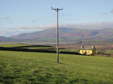 A green field with a telephone pole and a yellow house in the distance with hills in the background at Brookside in Grizebeck