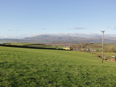 A green field with a yellow house and hills in the background at Brookside in Grizebeck