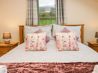 A bed with pillows and cushions between two wooden bedside tables with lamps at Brookside in Grizebeck