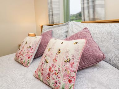 A bedroom with a bed featuring floral and bee patterned cushions and pink pillows at Brookside in Grizebeck