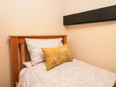 A single bed with patterned white bedding and a yellow floral cushion in a room with beige walls and a wooden beam at Brookside in Grizebeck