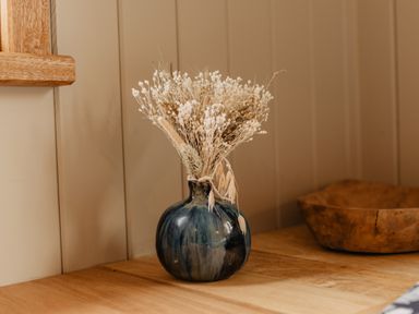 A dark blue vase with dried flowers on a wooden surface near a wooden bowl at Llethr - Shepherds Hut Llanbedr