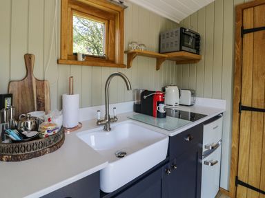 A kitchen corner with a white sink stainless steel faucet coffee machine kettle toaster and small oven at Llethr - Shepherds Hut in Llanbedr