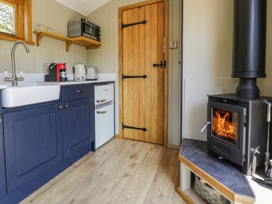 A kitchen area with blue cabinets a white sink small refrigerator and a wood burning stove at Llethr - Shepherds Hut in Llanbedr