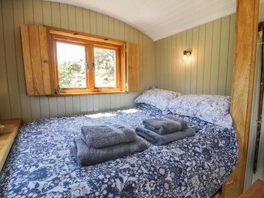 A bedroom with a bed covered in floral bedding and folded towels on top at Llethr - Shepherds Hut in Llanbedr