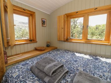 A bedroom with a bed folded towels and two wooden framed windows at Llethr - Shepherds Hut in Llanbedr