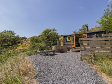 A wooden picnic table and hot tub outside a black wooden shepherds hut in a rural setting at Llethr - Shepherds Hut in Llanbedr