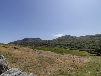 A landscape with grassy hills and rocky terrain under a clear blue sky at Llethr - Shepherds Hut in Llanbedr